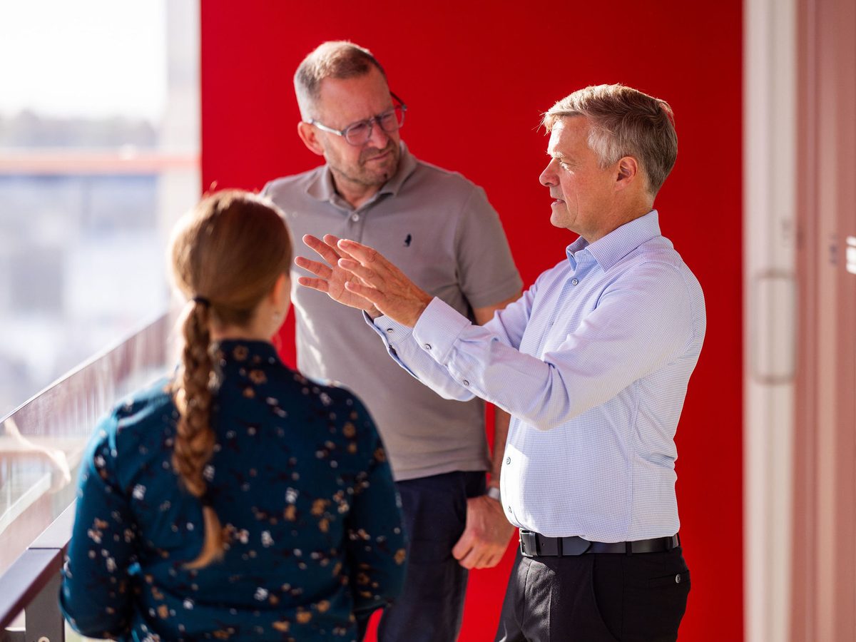 Jesper explaining something to two colleagues in front of a red wall
